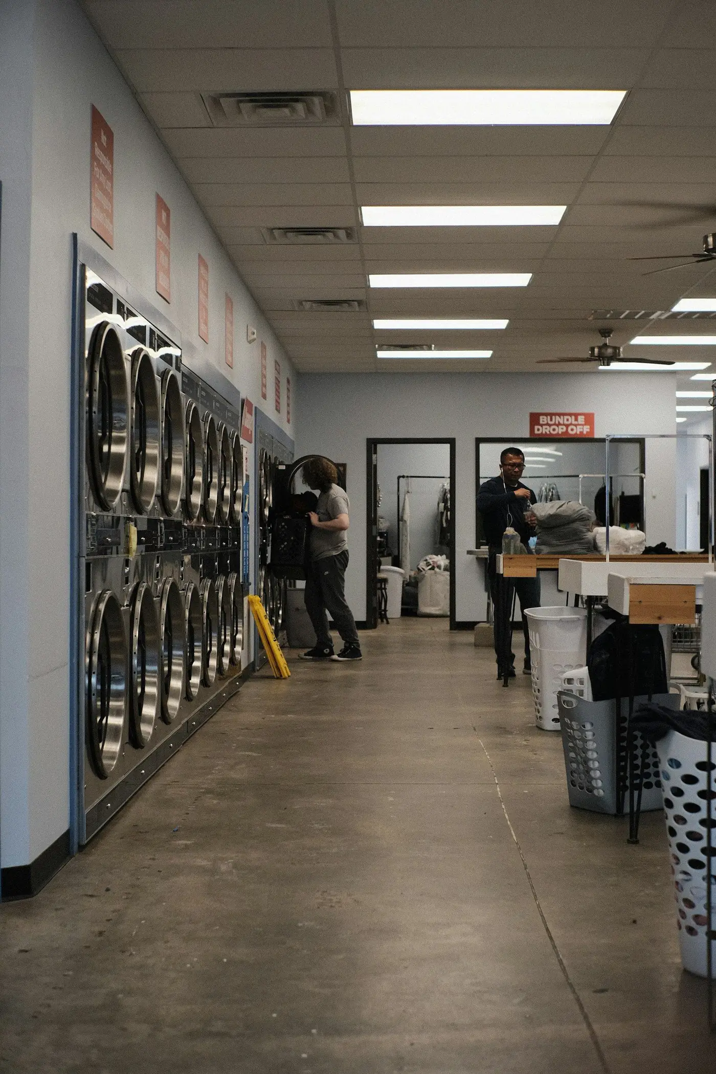 A long laundromat floor with staff working at the counter at the far end